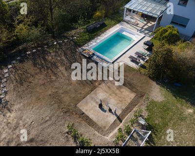 Volo con droni su un'area di terra fresca con erba coltivata accanto al cantiere di costruzione della piscina nel mese di aprile Foto Stock