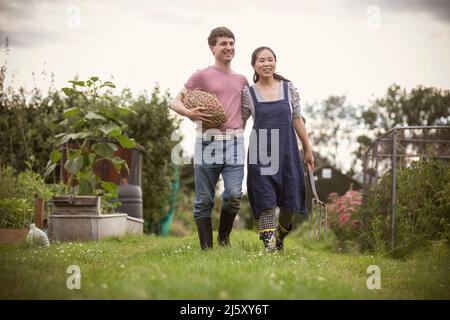 Coppia felice a piedi con verdure e forchetta in giardino Foto Stock