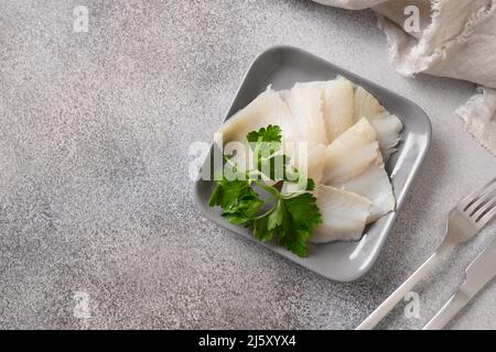 Deliziose fette di halibut affumicate servite con prezzemolo su sfondo grigio. Vista dall'alto. Spazio di copia. Foto Stock