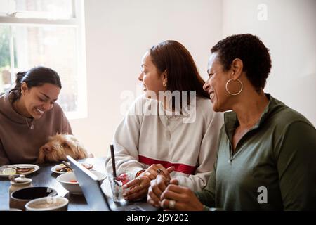 Madre e giovani figlie adulte con cane al tavolo da pranzo Foto Stock