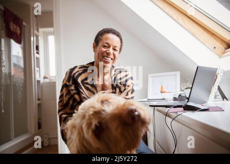 Ritratto donna felice con cane alla scrivania in ufficio a casa Foto Stock