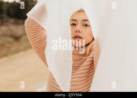 Donna in maglione rosa in piedi con braccio sollevato su strada asfaltata in campagna in luce diurna con testa di copertura in tessuto bianco Foto Stock