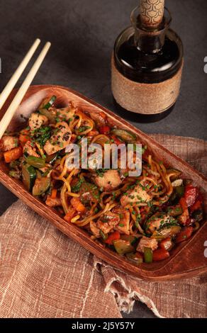 Da sopra di gustoso udon con verdure e pollo servito in piatto su tavola con bacchette e bottiglia di salsa di soia Foto Stock