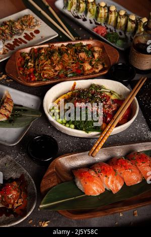 Dall'alto di vari sushi e poke serviti al tavolo con jiaozi tradizionale e udon con pollo al tavolo in ristorante asiatico Foto Stock
