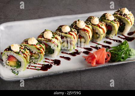 Dall'alto di deliziosi sushi rotolini con anguilla ricoperta di caviale nero e salsa unagi servita su foglia di banana verde su piatto bianco nel ristorante Foto Stock