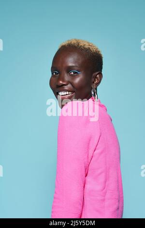 Ritratto di sorridente donna africana in rosa mentre si alza su sfondo blu in studio Foto Stock