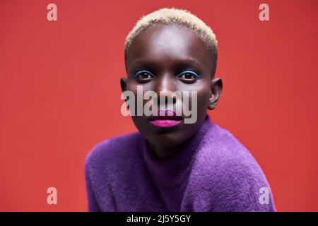 Ritratto di una giovane donna afro-americana che guarda la telecamera su sfondo rosso Foto Stock