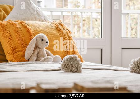 Raccolto di letto confortevole con cuscini colorati e un animale ripieno posto vicino alla finestra in una camera da letto luminosa Foto Stock