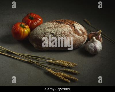 Pane di pane al forno quasi pomodori maturi posto su sfondo grigio con orecchie di grano in cucina Foto Stock