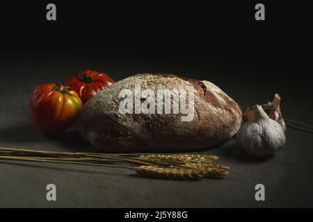 Pane di pane al forno quasi pomodori maturi posto su sfondo grigio con orecchie di grano in cucina Foto Stock