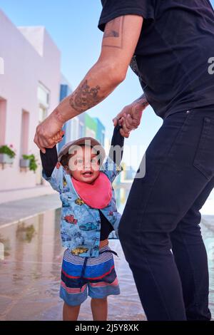 Il padre tiene le mani con il ragazzo grazioso del toddler sulla strada Foto Stock