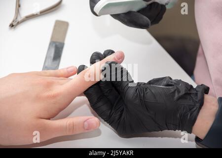 Mani gloved di un manicurist esperto che archivano le unghie di una donna giovane con una lima del chiodo. Mani durante una sessione di cura manicure in un salone di spa. Manicurista fi Foto Stock