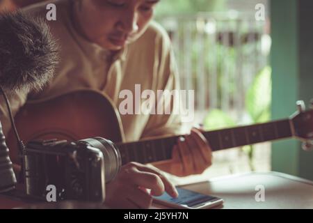 Il giovane asiatico suona la chitarra rilassandosi in un caffè. Foto Stock