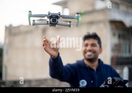 giovane indiano maschio cattura lancio drone pieghevole con fotocamera di mano con controller in altra mano sorridente mostrando l'aumento della produzione e. Foto Stock