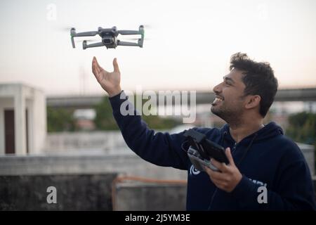 giovane indiano maschio cattura lancio drone pieghevole con fotocamera di mano con controller in altra mano sorridente mostrando l'aumento della produzione e. Foto Stock