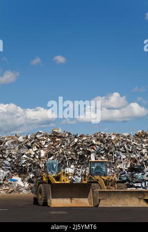 Caricatori frontali di fronte a una pila di articoli industriali e domestici in metallo scartati in un deposito per il riciclaggio dei rottami metallici. Foto Stock