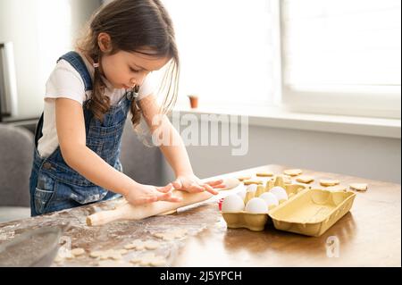 La ragazza del toddler cute che cucinano, impasta l'impasto, usando la spina di rotolamento, il bambino spende il tempo libero nel paese, cucinando i biscotti, godendo l'attività di fine settimana Foto Stock