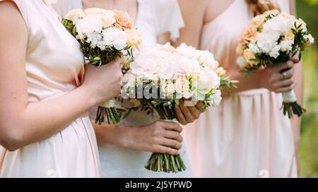 Concetto di matrimonio estivo. Bridesmaids in abiti avorio con mazzi da sposa da vicino all'aperto. Foto Stock