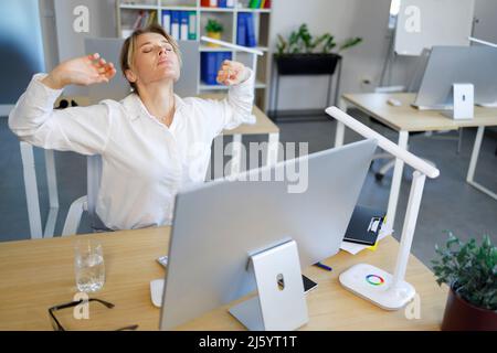 Donna d'affari di mezza età che si estende sul posto di lavoro in ufficio Foto Stock