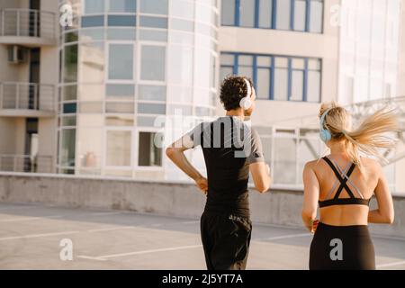 Giovane uomo e donna in cuffie che corrono insieme nel parcheggio all'aperto Foto Stock