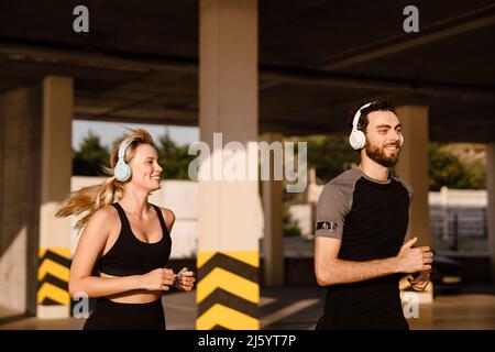 Giovane uomo e donna in cuffie che corrono insieme nel parcheggio all'aperto Foto Stock