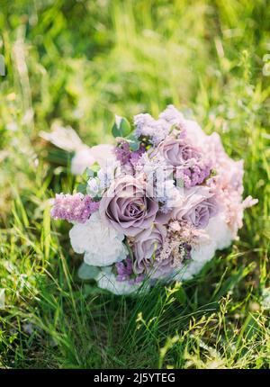 Bouquet di nozze con teneri rose bianche e fiori di lilla su erba verde fresca. Bouquet viola nuziale su sfondo verde lussureggiante erba primo piano. Molla Foto Stock