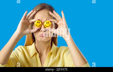 Donna triste cercando di falsificare la felicità, tenendo felici emoji e nascondendo le sue emozioni reali Foto Stock