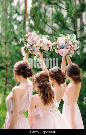 Bridesmaids in abiti rosati con mazzi da sposa all'aperto su sfondo verde. Felice estate matrimonio concetto. Foto Stock