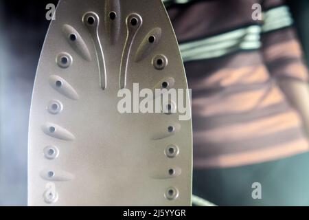 Una donna casalinga tiene un ferro caldo in mano con il vapore. La lavanderia è stirare il concetto di uno stile di vita moderno, una donna che ferra c Foto Stock