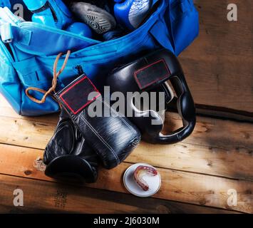 Casco da boxe e guanti neri. Munizioni di pugilato su sfondo di legno. Borsa sportiva e guanti da boxe. Tasto basso. Foto Stock