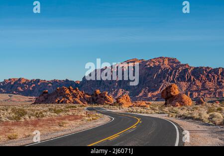 Overton, Nevada, USA - 24 febbraio 2010: Valle del fuoco. Paesaggio al tramonto sotto il cielo blu con strada asfaltata nera che percorre il deserto asciutto con r Foto Stock