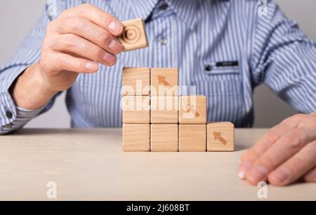 Uomo costruzione scala carriera da blocchi di legno con frecce. Sviluppo e crescita del business. Concetto di motivazione. Raggiungere gli obiettivi in alto. Foto di alta qualità Foto Stock