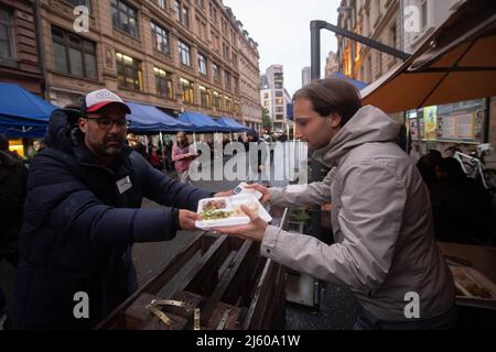 26 aprile 2022, Hessen, Francoforte sul meno: I dipendenti consegnano cibo al Bahnhofsviertel durante la rottura del digiuno del 5th organizzata dall'iniziativa gemeinsames Fastenbrechen. Nella sezione di Elbestraße tra Münchenerstrasse e Kaiserstraße, gli uomini d'affari e i ristoranti locali invitano la gente a condividere un pasto. Il mese del digiuno islamico del Ramadan continua fino alla sera del 1 maggio 2022. Foto: Sebastian Gollnow/dpa Foto Stock