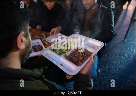 26 aprile 2022, Hessen, Francoforte sul meno: La gente passa il cibo l'una all'altra durante la rottura 5th del digiuno dell'iniziativa gemeinsames Fastenbrechen nel Bahnhofsviertel. Nella sezione Elbestraße tra Münchenerstrasse e Kaiserstraße, gli uomini d'affari e i ristoranti locali invitano la gente a condividere un pasto. Il mese del digiuno islamico del Ramadan continua fino alla sera del 1 maggio 2022. Foto: Sebastian Gollnow/dpa Foto Stock