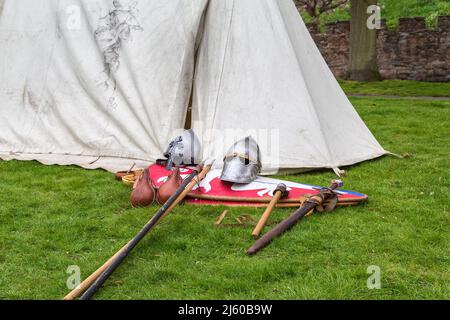 I caschi, gli scudi e le armi dei cavalieri medievali posati sull'erba da una tenda. Parte di un campo di storia vivente della società storica. Foto Stock