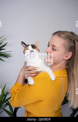 giovane donna bionda che porta il suo gatto calico che è completamente dispiaciuto guardando la macchina fotografica angry con spazio copia Foto Stock