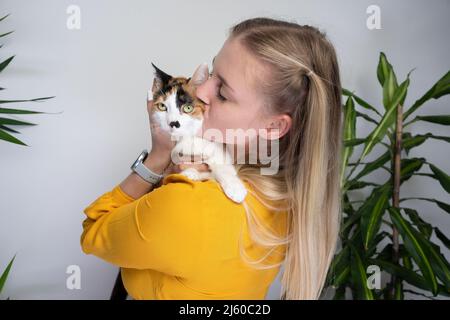 giovane donna che porta il suo gatto calico abbracciando e baciando il gattino che è dispiaciuto di esso Foto Stock