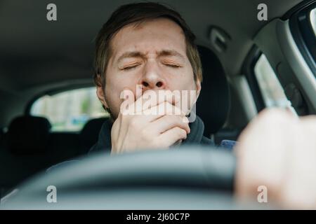 Primo piano ritratto sonnolento giovane conducente yawning sul sedile anteriore della vettura. Foto Stock