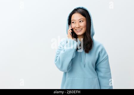 Bella felice Coreano giovane femmina in blu Hoodie tenere telefono parla con il ragazzo posa isolato su sfondo bianco studio. La migliore offerta Foto Stock