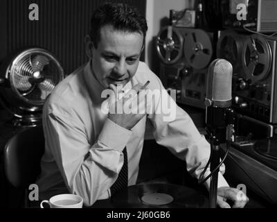 Un DJ radio retrò degli anni '50 suona la musica mentre tiene il record e la sigaretta. Una classica immagine in bianco e nero di un'epoca passata. Nostalgia. Foto Stock