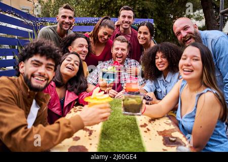 Gruppo di selfie di persone che si divertono e si divertono. Amici allegri multirazziali che bevono e tostano cocktail al bar della birreria fotografando insieme Foto Stock