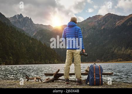 vista posteriore del fotografo asiatico che guarda il tramonto sulle montagne Foto Stock