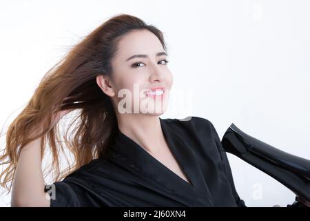 Giovane e bella donna cinese usando un asciugacapelli per asciugare i capelli, su sfondo bianco - foto di scorta Foto Stock