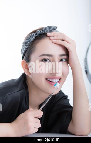 Giovane donna cinese energica che usa uno spazzolino da denti per pulire e sbiancare i suoi denti su base quotidiana, su sfondo bianco - foto di scorta Foto Stock