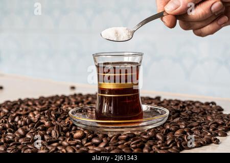 la mano mette un cucchiaino di zucchero in un bicchiere di vetro con caffè. Foto Stock