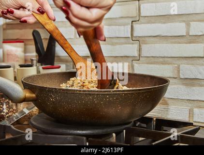 Lo chef prepara le spatole in legno in una padella con patate fritte, castagne, prezzemolo, parmigiano su una stufa a gas. Ricetta passo dopo passo Foto Stock