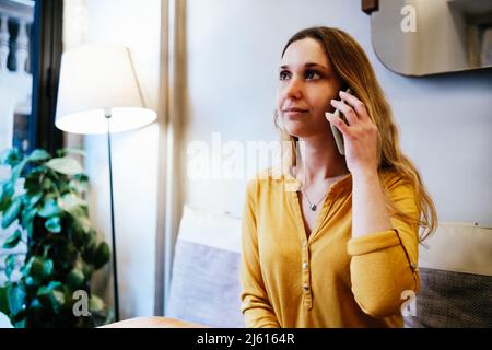 giovane donna bionda attraente con camicia gialla che parla al telefono in una caffetteria Foto Stock