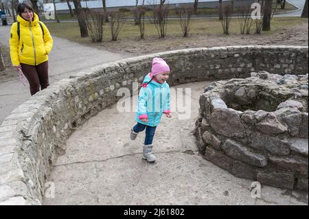 Una ragazza con pigtail lunghi corre intorno ad una fontana asciutta vuota. Una donna in un kurta giallo sta guardando un bambino. Una madre e sua figlia passeggiare attraverso t Foto Stock