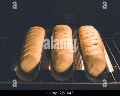 l'immagine mostra 3 baguette fatte in casa o pane francese in una speciale padella di baguette situata nel forno di cottura durante il periodo di cottura Foto Stock