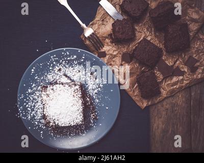 vista dall'alto di brownie fatte in casa su un rustico tavolo in legno decorato con carta da forno e forchetta e coltello in argento sterling Foto Stock